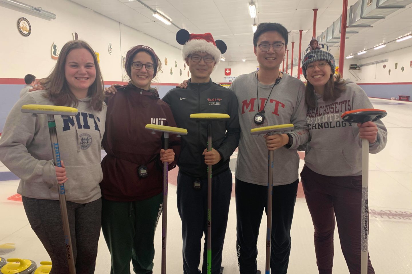 Curling students posing on ice holding brooms