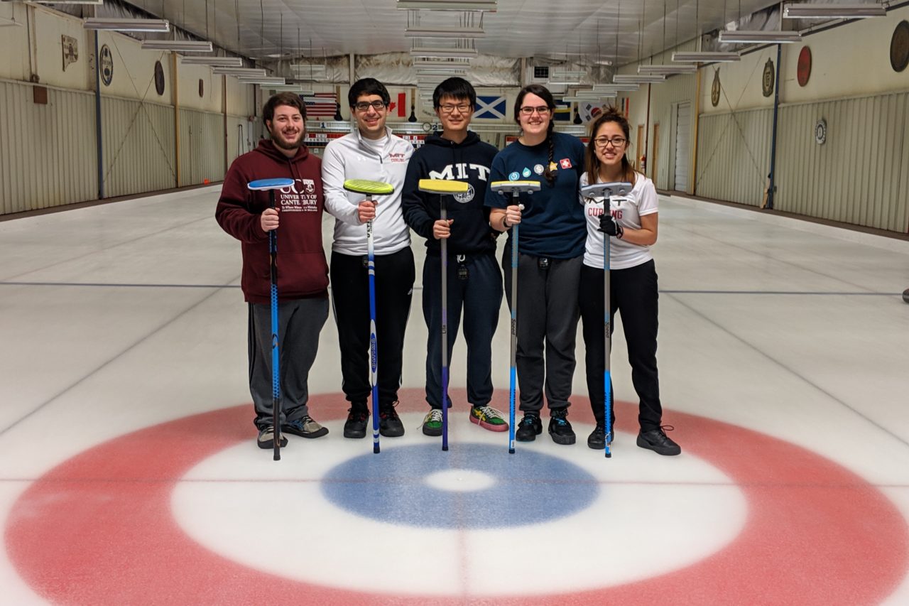Curling students posing on ice holding brooms
